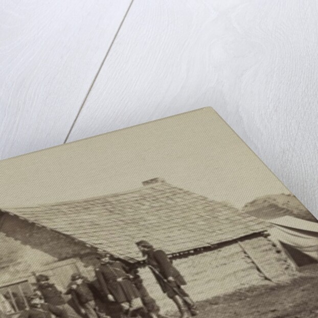 A group of soldiers, and two young men, one an African American, stand outside of log cabin quarters by American Photographer
