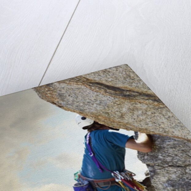 Young man rock climbing up a vertical cliff by Anonymous