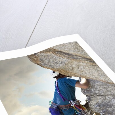Young man rock climbing up a vertical cliff by Anonymous