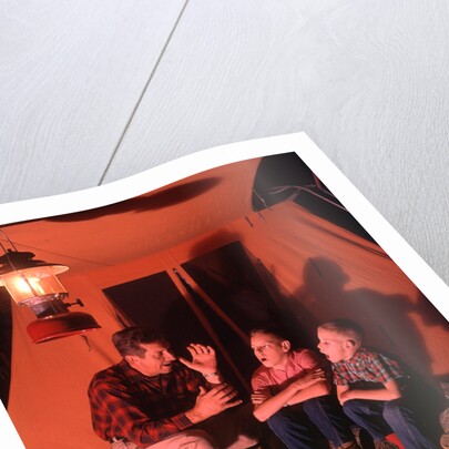 1960s 1970s Grandfather Telling Scary Story To Boys By Tent At Night Campsite In Shadows by Anonymous
