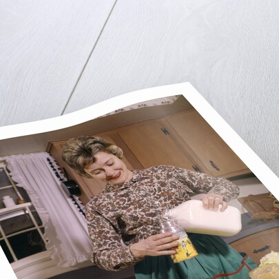 1960s Woman Housewife Mother Wearing Apron In Kitchen Pouring Milk Into Thermos For School Lunch by Anonymous