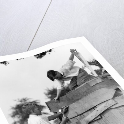 1930s Pair Of Boys Building Shack One Nailing Board To Side One On Roof With Saw by Anonymous