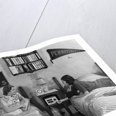 1930s 1940s Two Teen Girls Lying On Dormitory Beds Room Mates Listening To Radio College School Pennants On Wall by Anonymous