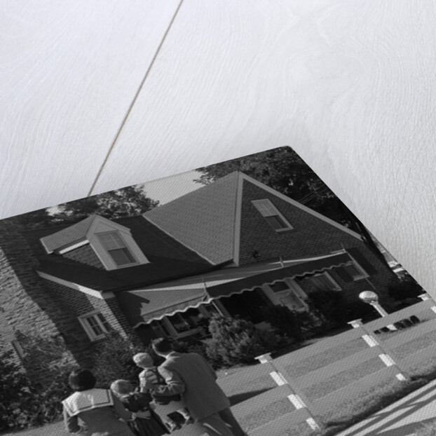 1950s Family Standing By White Fence Looking At Brick House by Anonymous