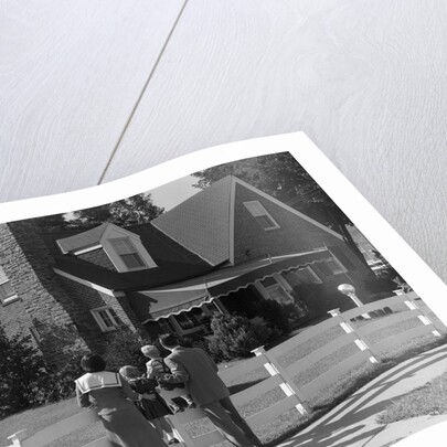 1950s Family Standing By White Fence Looking At Brick House by Anonymous