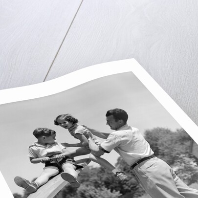 1950s Father Lifting Son And Daughter Onto A Playground Seesaw Outdoor by Anonymous