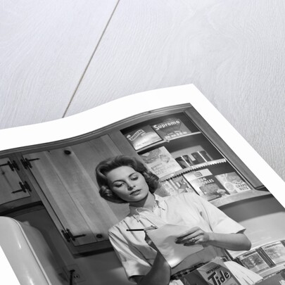 1960s Woman Housewife In Kitchen Checking Grocery Food Shopping List by Anonymous