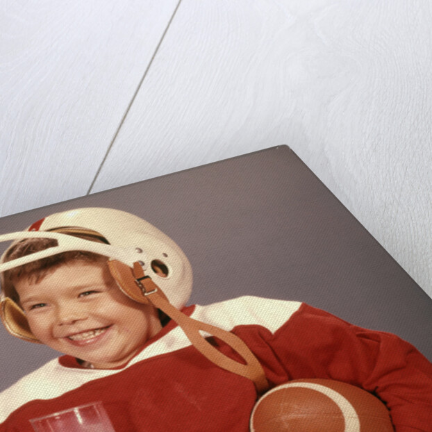1950s 1960s Boy Drinking Milk Wearing Football Helmet Red Jersey Holding Ball by Anonymous