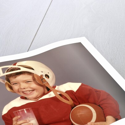 1950s 1960s Boy Drinking Milk Wearing Football Helmet Red Jersey Holding Ball by Anonymous