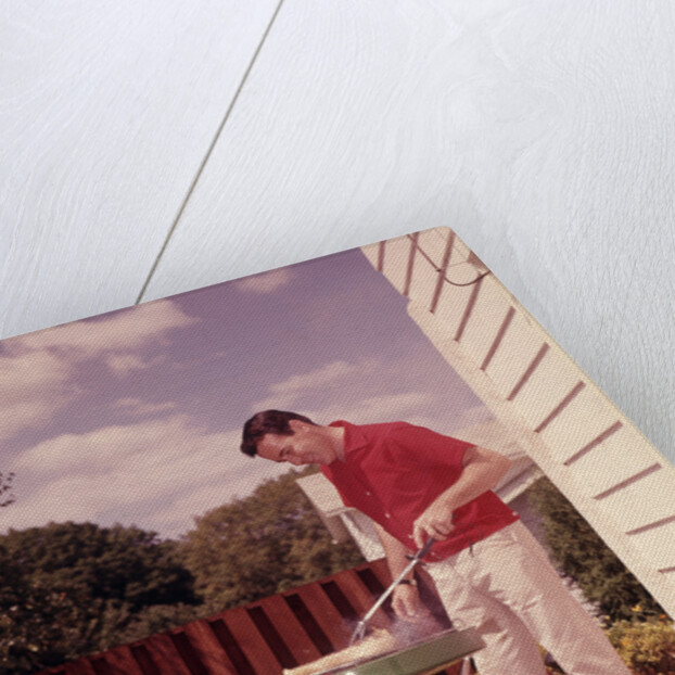 1960s Man Wearing Red Shirt Cooking Steak Outdoor On Backyard Grill by Anonymous
