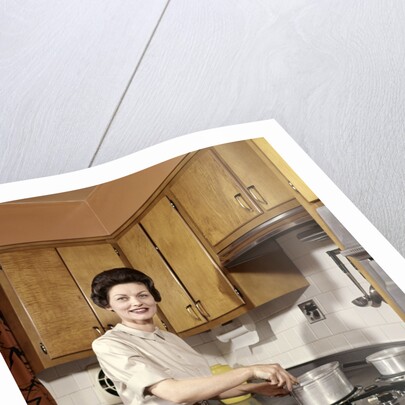 1960s Woman Housewife Wearing An Apron Stirring Cooking Pot At Kitchen Stove by Anonymous