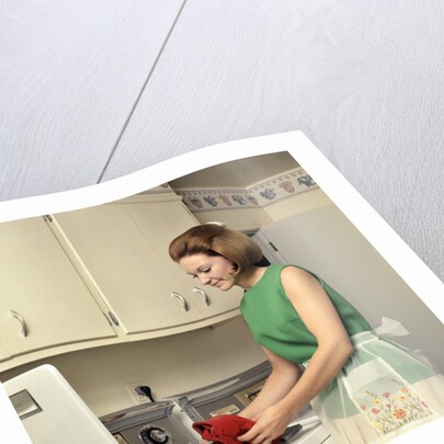 1970s Woman Housewife Homemaker Wearing Apron Loading Laundry Into Washing Machine by Anonymous
