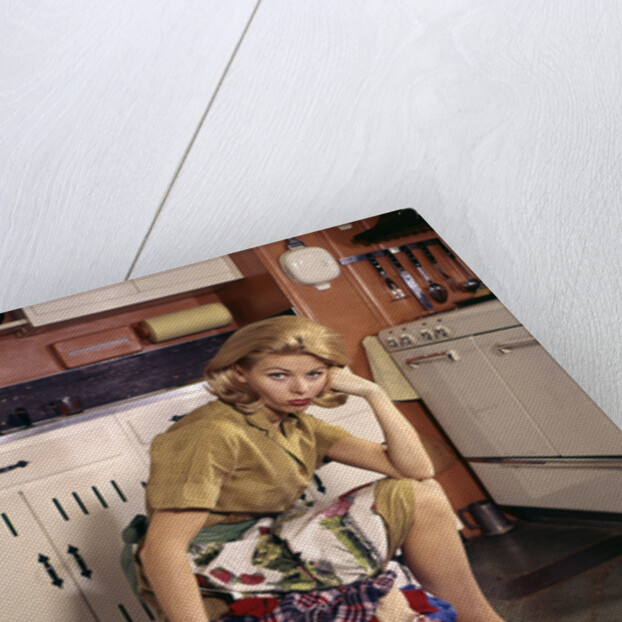 1960s Weary Dejected Woman Housewife Homemaker Sitting On Full Laundry Basket In Kitchen by Anonymous