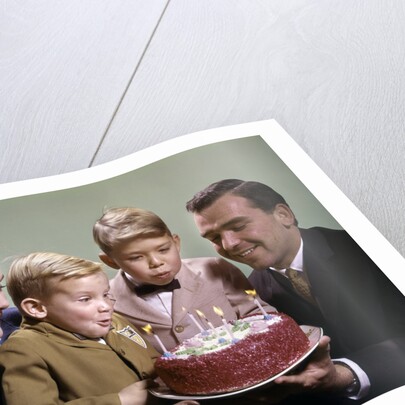 1960s Mother And Father Holding Birthday Cake And Sons Blowing Out Candles by Anonymous