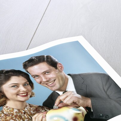 1950s 1960s Young Couple Man And Woman Put Quarter In Savings Piggy Bank by Anonymous