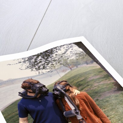 1970s Young Romantic Teenage Couple Man Woman Wearing Gas Masks Walking By River by Anonymous