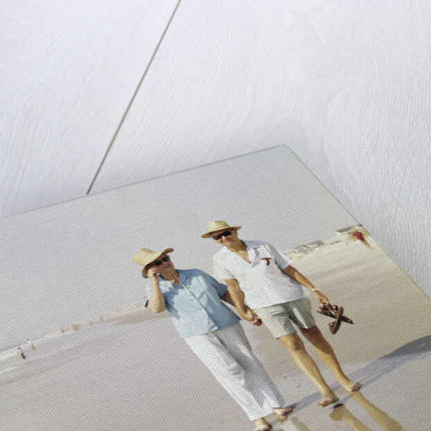 1970s Senior Couple Walking Beach Holding Hands Wearing Straw Hats by Anonymous