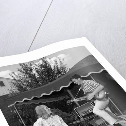 1960s Boy Playing Guitar, Woman Holding Soft Drink Bottle Outside In Backyard by Anonymous
