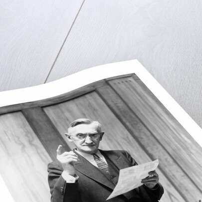 1930s Elderly Man In Office Standing Behind Desk Gesturing With Raised Finger by Anonymous