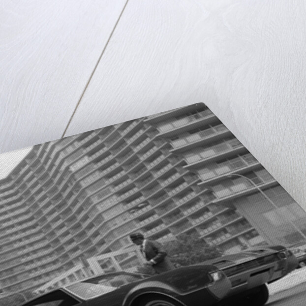 1960s Man In Suit and Hat Standing Beside Oldsmobile Toranado In Front Of Large Apartment Building by Anonymous
