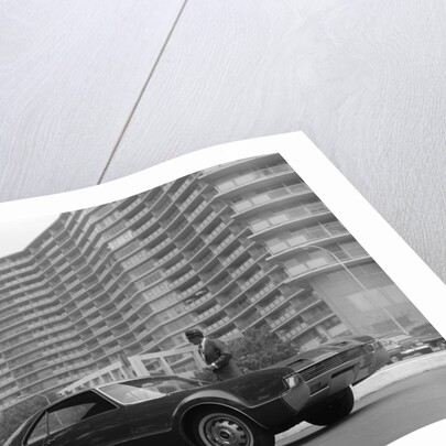1960s Man In Suit and Hat Standing Beside Oldsmobile Toranado In Front Of Large Apartment Building by Anonymous