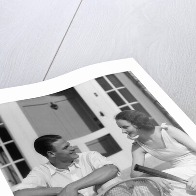 1930s Couple Man Woman In Tennis Whites Holding Racquets Sitting Talking On Steps In Front Of House Outdoor by Anonymous