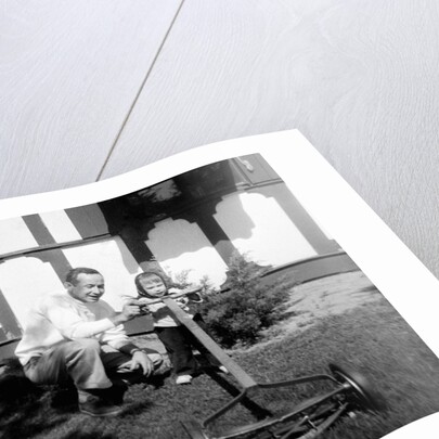A father show his two year old daughter how to mow the lawn, ca. 1956 by Anonymous