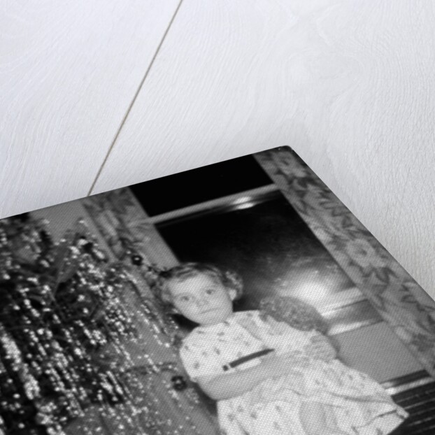 A little girl stands by the Christmas tree clutching her doll, ca. 1955 by Anonymous