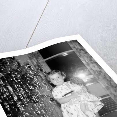 A little girl stands by the Christmas tree clutching her doll, ca. 1955 by Anonymous