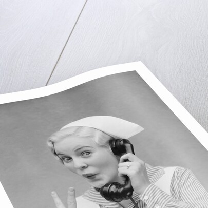 Smiling blond nurse with surprised expression talking on telephone holding up two fingers by Anonymous
