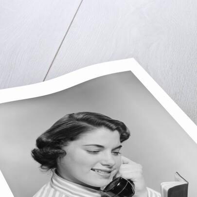 Young woman talking on telephone reading address from little black book by Anonymous
