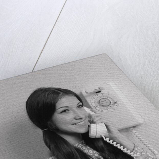 Smiling teenage girl talking on rotary wall telephone by Anonymous