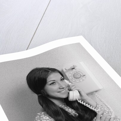 Smiling teenage girl talking on rotary wall telephone by Anonymous