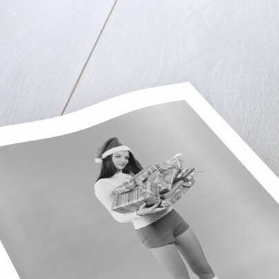 Young woman wearing santa claus hat hot pants go-go boots holding wrapped christmas presents by Anonymous