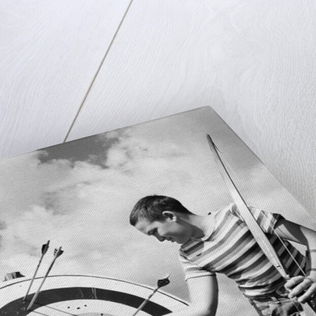 Boy jeans striped t-shirt holding bow & pulling arrow out of target bull's-eye by Anonymous