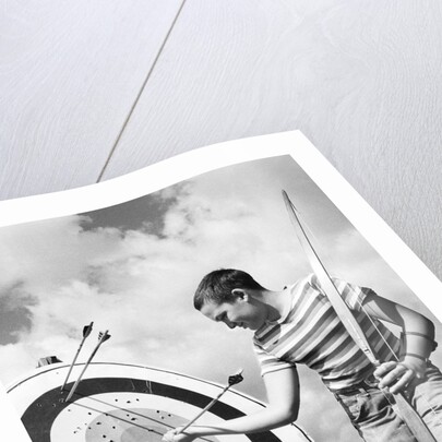 Boy jeans striped t-shirt holding bow & pulling arrow out of target bull's-eye by Anonymous
