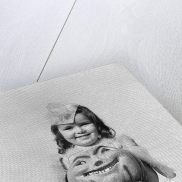 Happy smiling little girl in costume holding a papier-mache pumpkin head by Anonymous