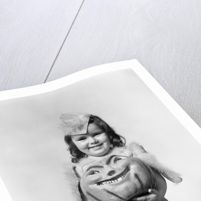 Happy smiling little girl in costume holding a papier-mache pumpkin head by Anonymous