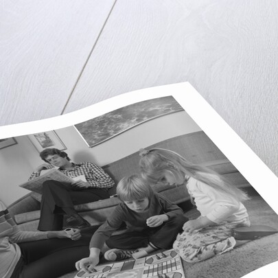 Family mother kids playing board game living room floor father reading newspaper by Anonymous