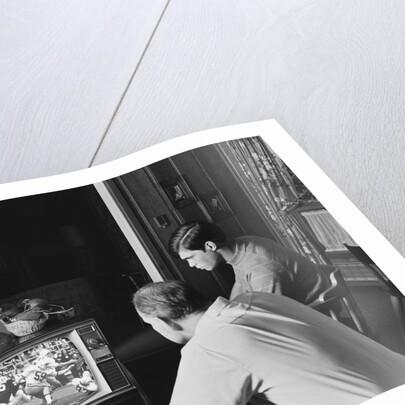 Teen boy watching football game on television with adult dad by Anonymous