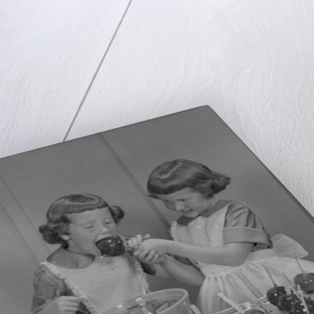 Two twin girls eating making candy apples in kitchen by Anonymous