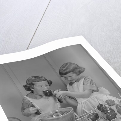 Two twin girls eating making candy apples in kitchen by Anonymous