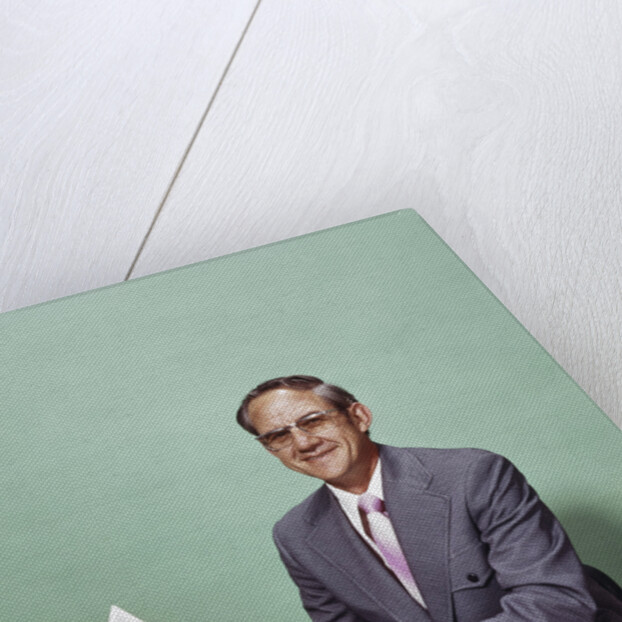 Smiling man at desk holding papers with mortgage officer sign looking at camera by Anonymous
