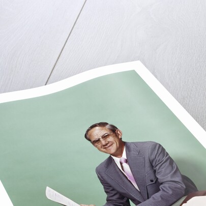 Smiling man at desk holding papers with mortgage officer sign looking at camera by Anonymous