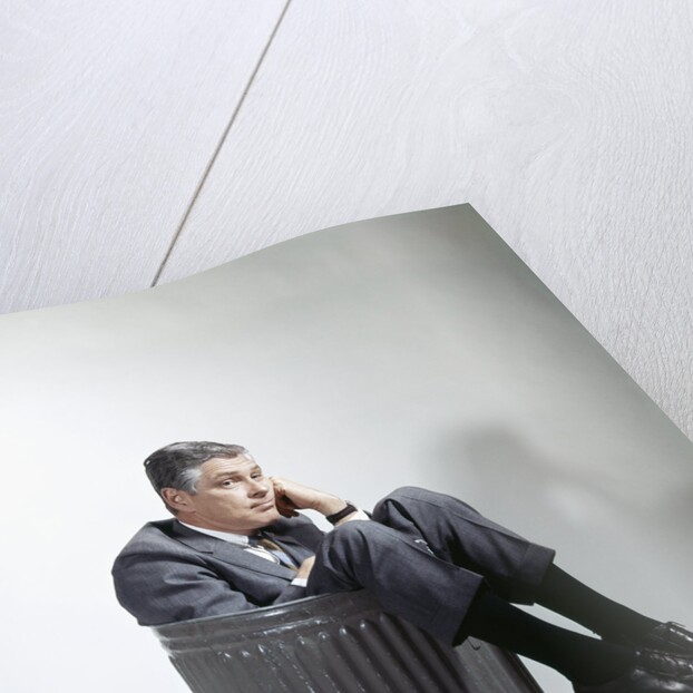 Sad man in business suit sitting in trash garbage can by Anonymous