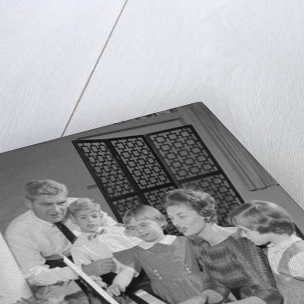 Family standing around piano singing by Anonymous