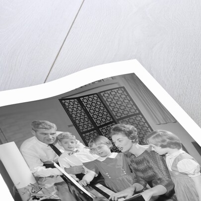 Family standing around piano singing by Anonymous