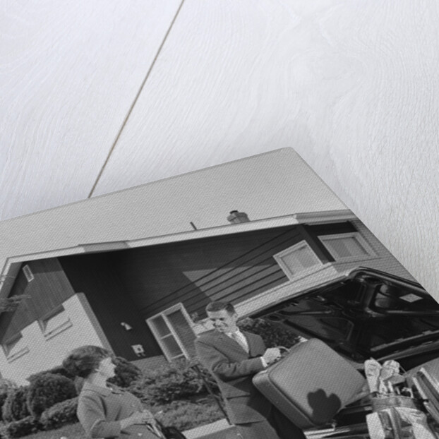 Couple man woman packing luggage into car trunk by suburban house by Anonymous