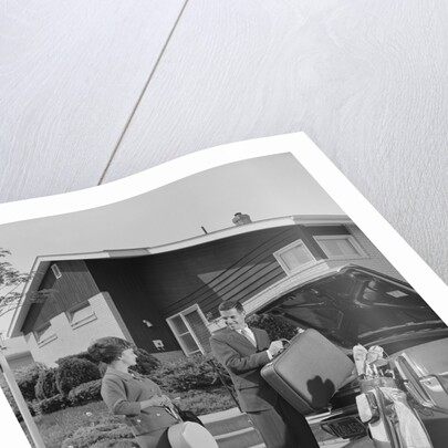 Couple man woman packing luggage into car trunk by suburban house by Anonymous