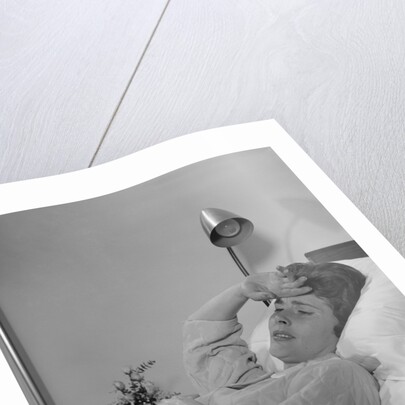 Ailing woman patient lying in hospital bed hand pressed to forehead by Anonymous